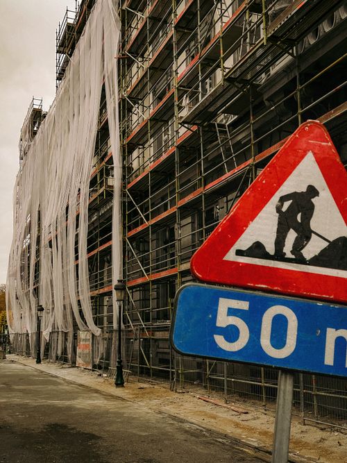 Free Construction scene showing scaffolding and a caution sign in an urban area, emphasizing ongoing development. Stock Photo