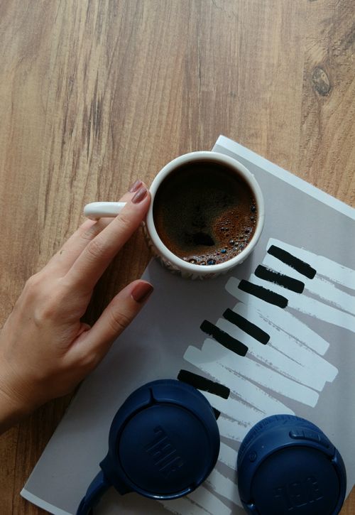 Free Top view of a hand holding a coffee cup with headphones on a wooden table, suggesting a cozy morning routine. Stock Photo