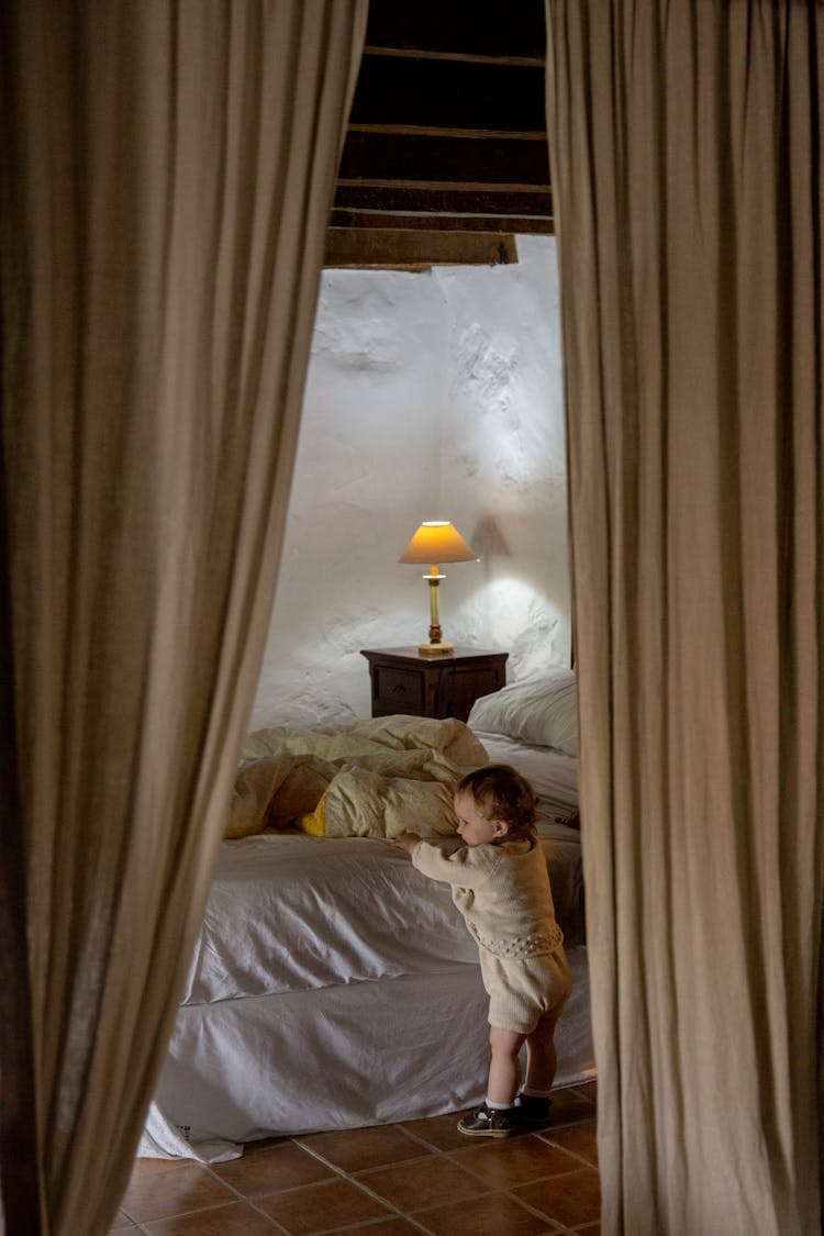 Adorable Toddler Standing Alone Near Bed In Rural Interior House