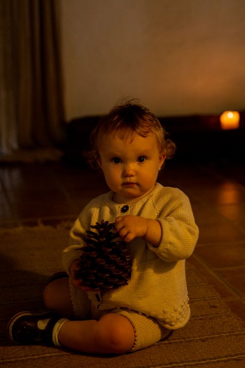 Free Adorable toddler girl in casual clothes sitting on floor carpet playing with big bump in dark light inside rural room and looking at camera Stock Photo