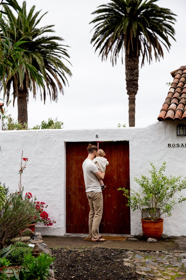 Young Man With Little Child Near Stone Fence Door Inside Backyard At Countryside