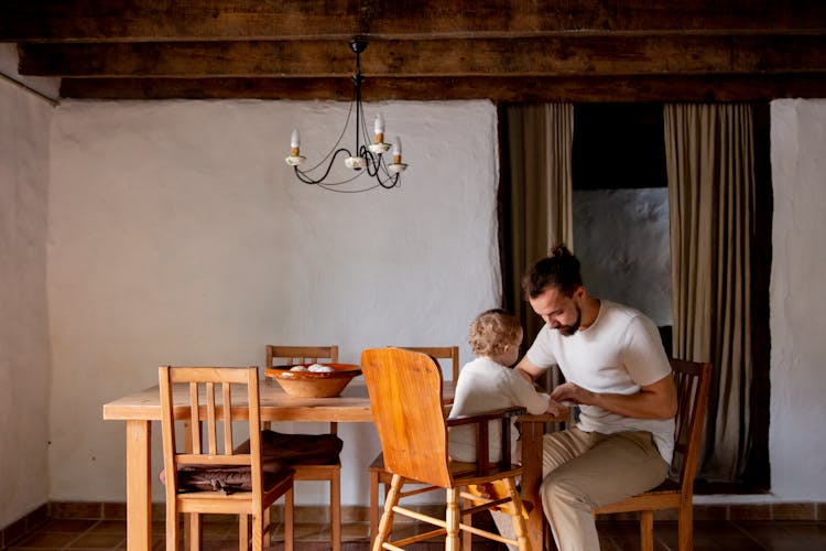 Focused Young Man With Toddler Girl Sitting At Desk In Rural Interior House