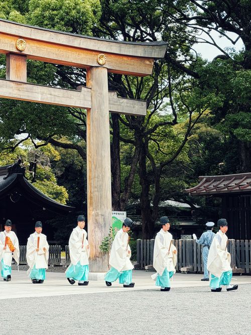 Free Japanese priests in traditional attire passing under a torii gate at Meiji Shrine, Tokyo. Stock Photo