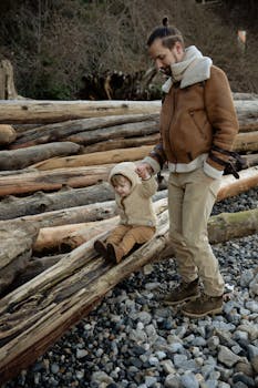 秋天，积极的父亲穿着温暖的外套，牵着小女儿的手沿着岩石海岸散步，并在木头上玩耍