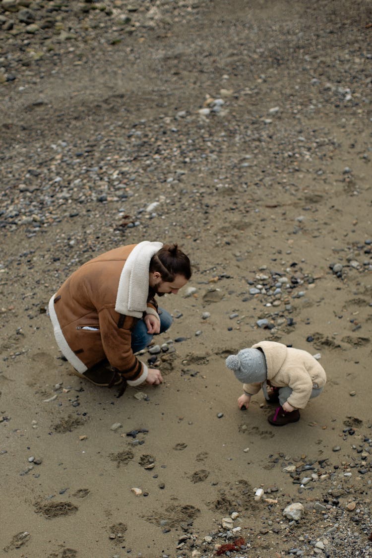 Father And Child Collecting Stones On Beach