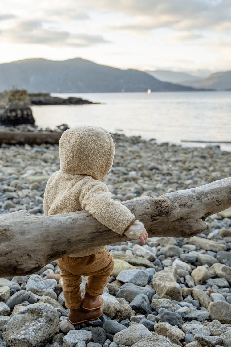 Cute Little Kid Leaning On Log While Resting On Rocky Coast