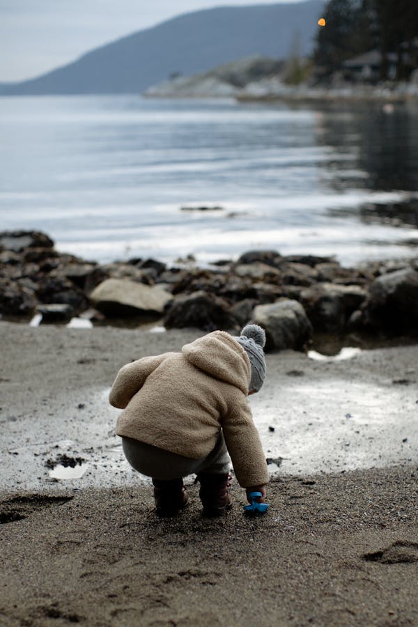 Little kid playing with toy on wet shore in overcast day during weekend