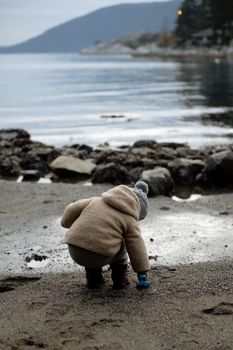 Little kid playing with toy on wet shore in overcast day during weekend