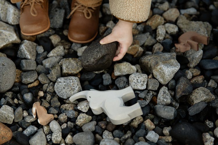 Unrecognizable Crop Kid Playing With Toys And Stones On Rocky Ground