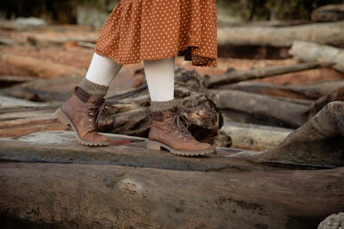 Unrecognizable crop woman wearing warm casual boots and skirt walking on log while spending time in countryside during weekend trip in autumn