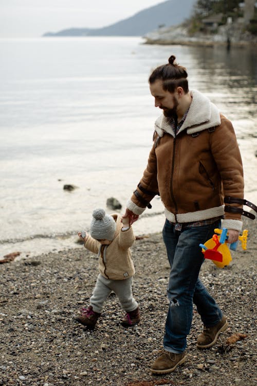 Père Transportant Des Jouets En Marchant Avec Petit Enfant Sur La Plage Près De L'eau