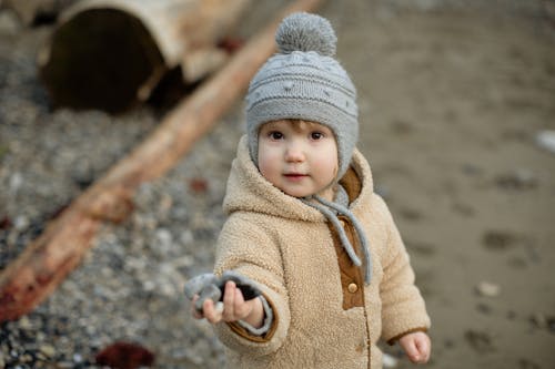 Child In Brown Coat And Gray Knit Cap Holding Rocks