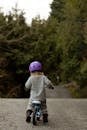 一个孩子戴着紫色头盔，骑着三轮车沿着宁静的森林小路行驶