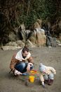 Cheerful bearded father in warm outerwear playing with little kid with toy shovel and busket in sand while spending time together on beach during weekend