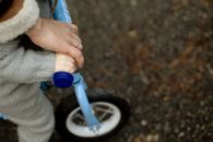 From above unrecognizable crop father teaching little kid how to ride bicycle on wet asphalt road during walk together in autumn day