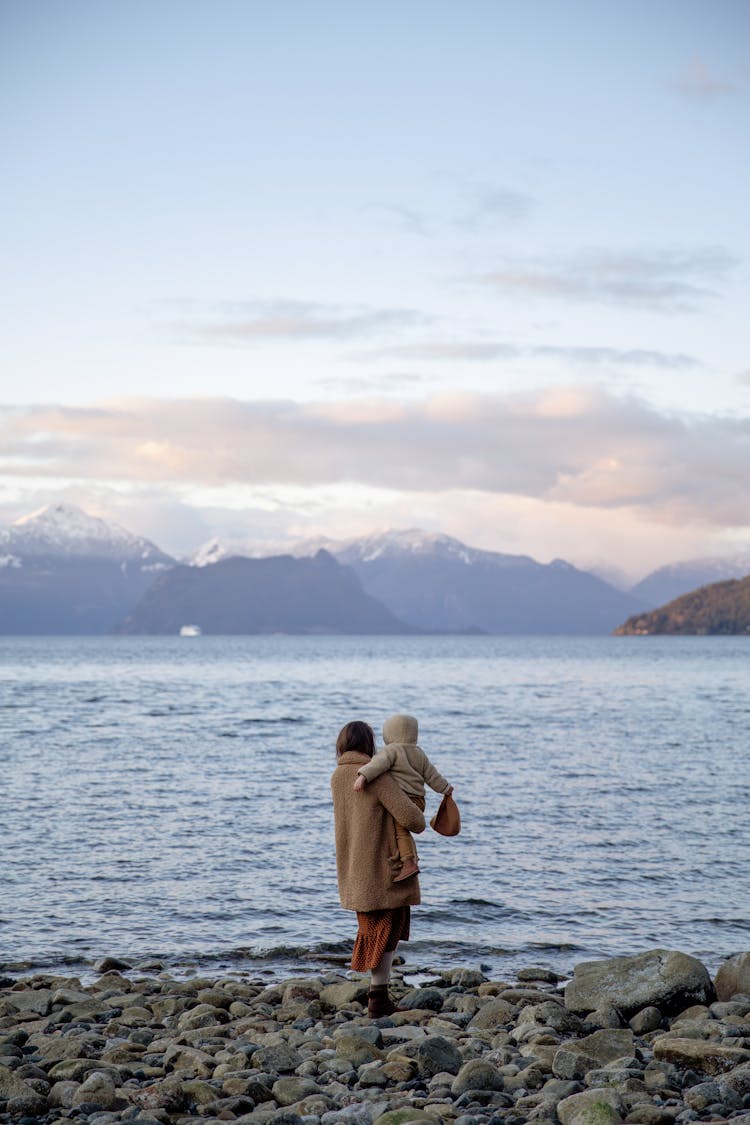 Anonymous Mother Holding Kid On Hands While Standing On Rocky Coast