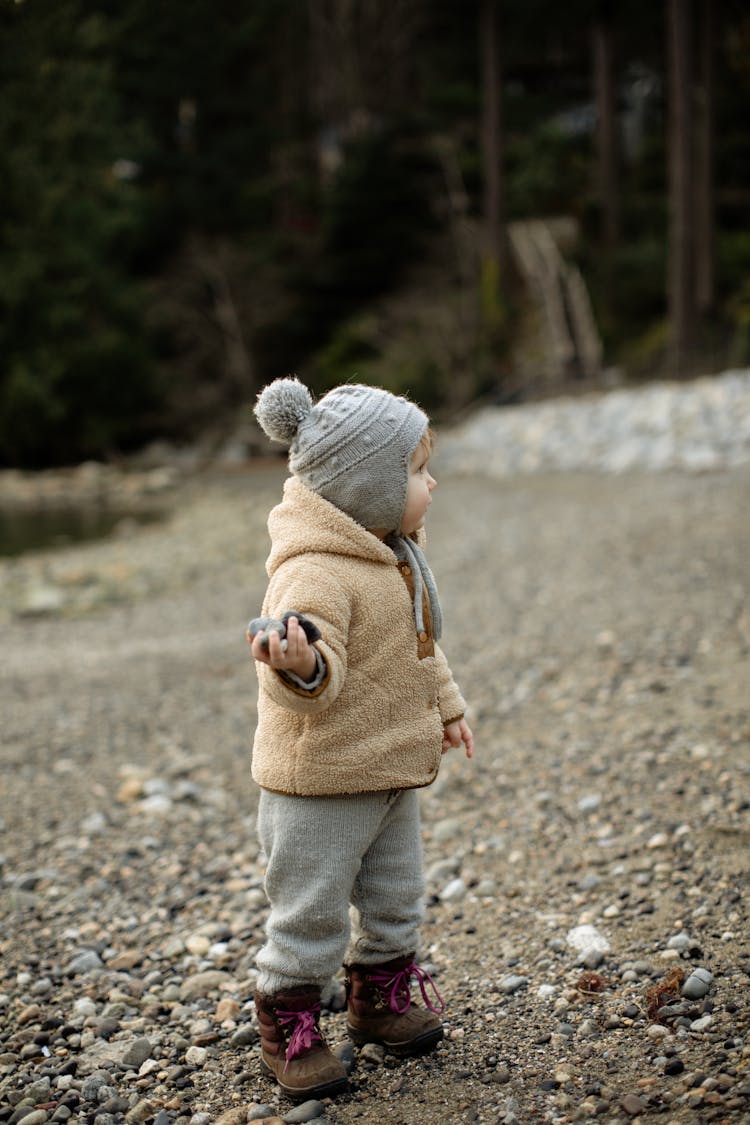 Cute Little Kid Standing On Stony Ground With Pebbles In Hand