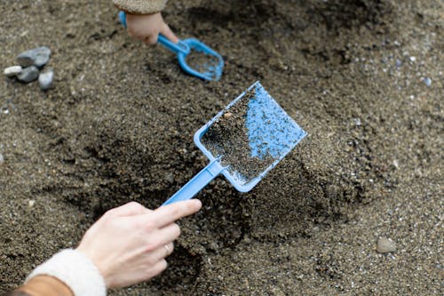 Free Crop faceless mother with baby playing with plastic shovels in sand Stock Photo