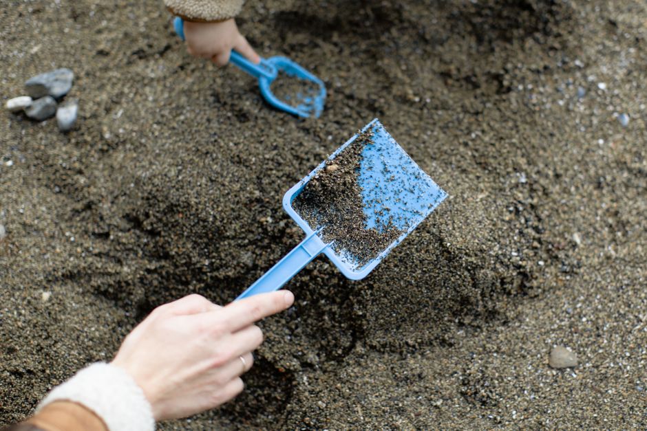 From above of unrecognizable person and little child in warm clothes playing with sand while spending time together near sea