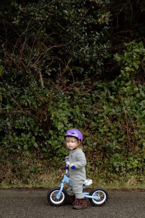 Adorable little girl riding bicycle on sidewalk against thickets of forest