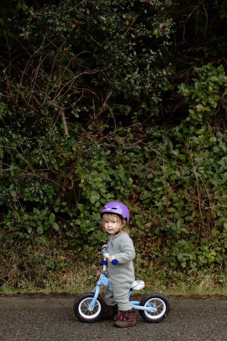 Adorable Little Girl Riding Bicycle On Sidewalk Against Thickets Of Forest