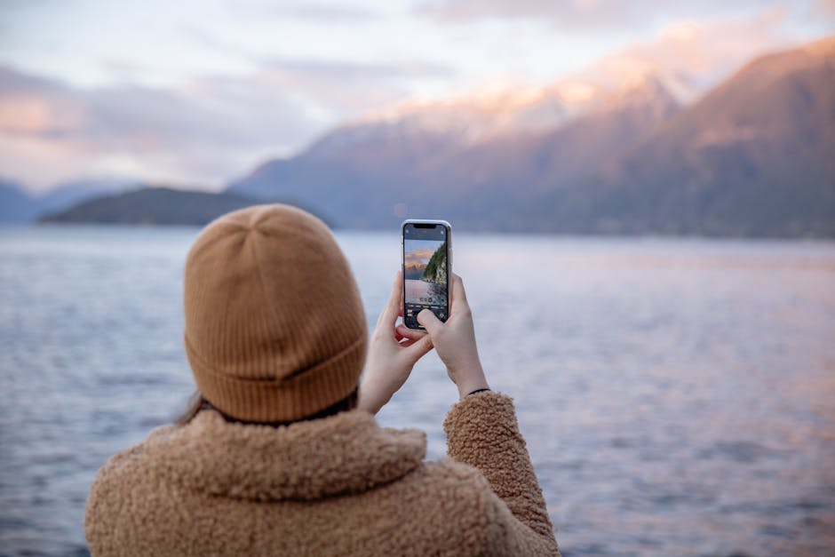 Unrecognizable female traveler taking photo of lake and mountains