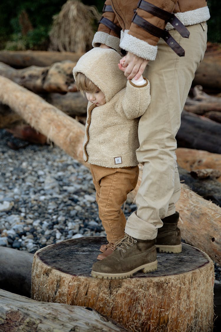 Crop Person Standing Adorable Kid On Wooden Logs In Seashore