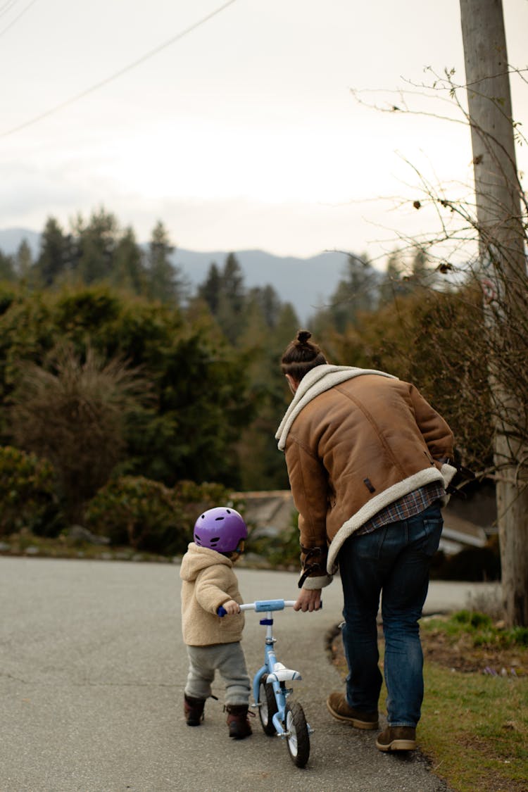 Full Body Of Father And Child In Protective Helmet Pushing Bike Along Road