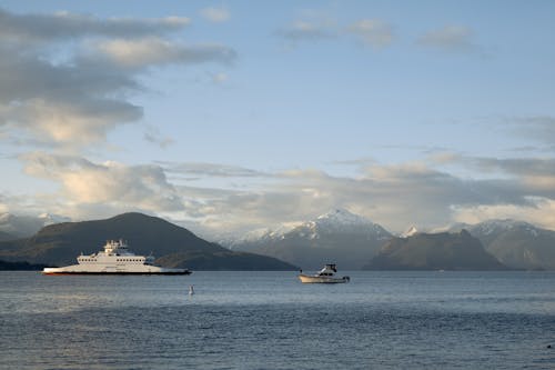 Small boats on calm rippled seawater against mountains with snowy peaks and cloudy sky in winter during sunset