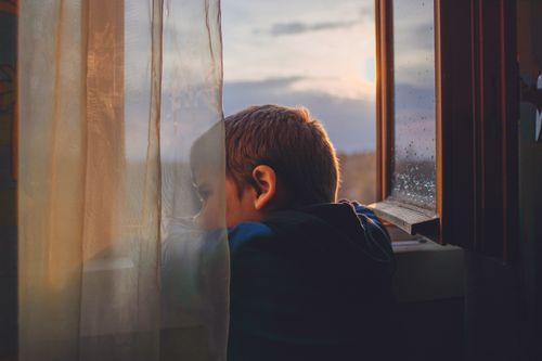 Free Young boy looking through window, captured during a tranquil sunrise indoors. Stock Photo