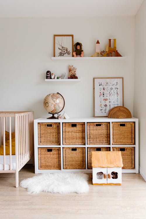 Free Comfortable bed with toys globe and paintings placed on wooden cabinet with wicker boxes and soft white rug with toy house on floor Stock Photo