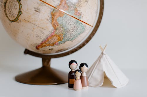 Free From above of miniature toys tipi house and American Indian family placed near vintage globe against gray background at daytime Stock Photo
