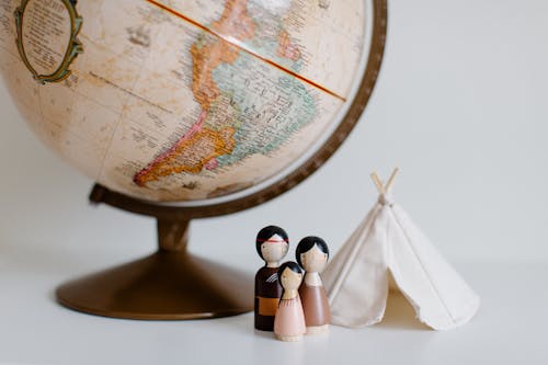 From above of miniature toys tipi house and American Indian family placed near vintage globe against gray background at daytime