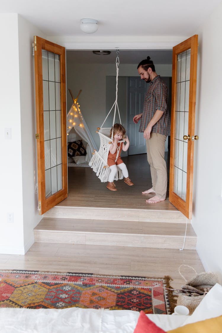 Casual Father Helping Daughter With Swing At Home