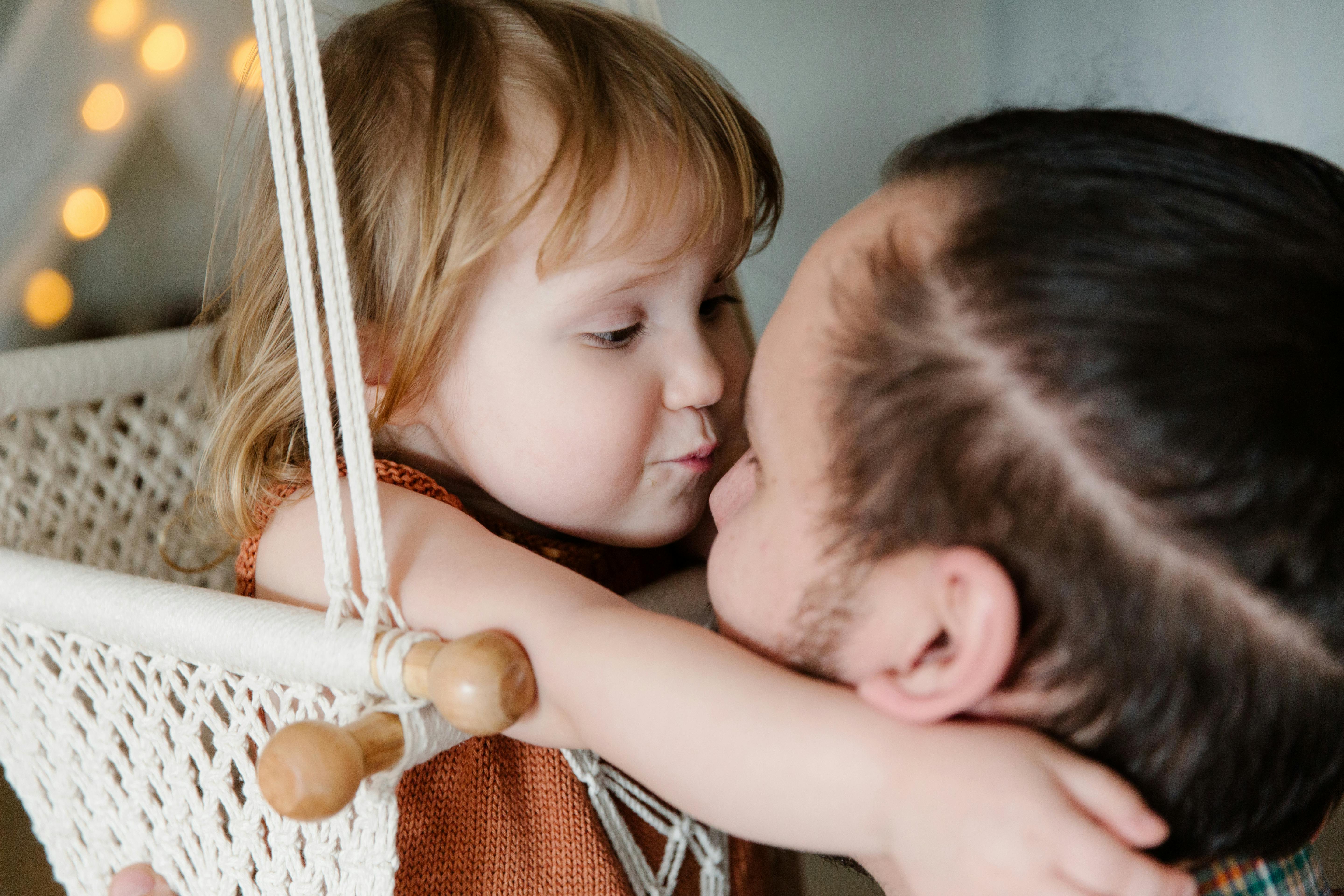 cute kid hugging father while resting in hanging swing at home