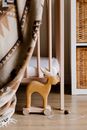 From above of wooden deer toy with rope on floor placed near cozy plaid on bed in light nursery room at home
