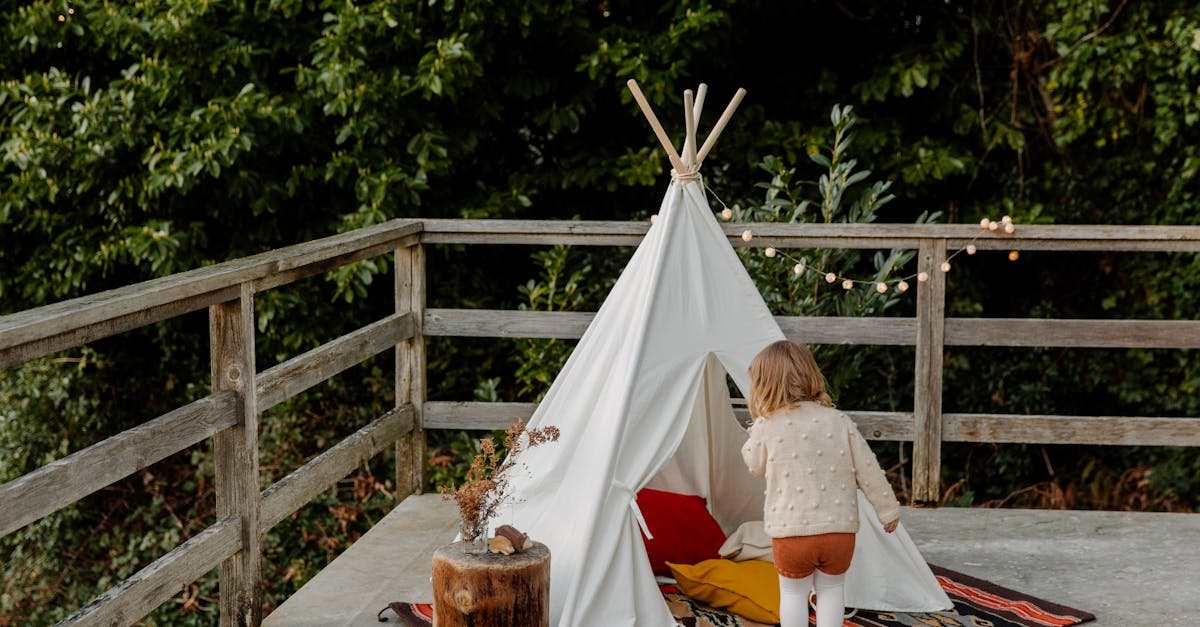 Back view of little child standing at entrance to boho tent placed on wooden terrace
