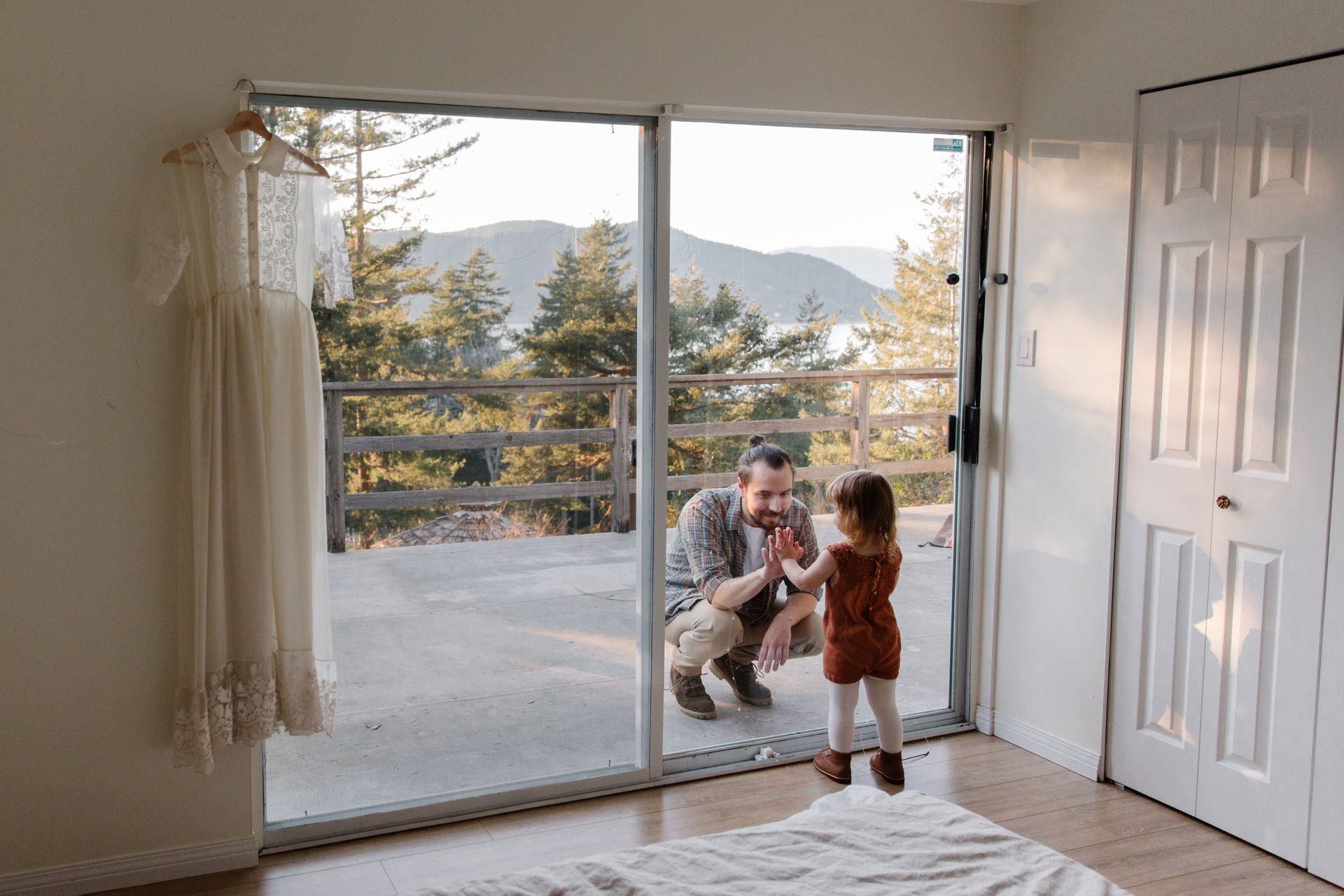 A father and daughter engage in a playful moment at home, separated by a glass door with a scenic mountain view.