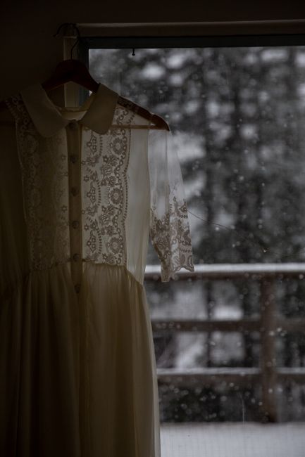 Old fashioned light white dress with lace and buttons hanging on hanger by window in rainy day
