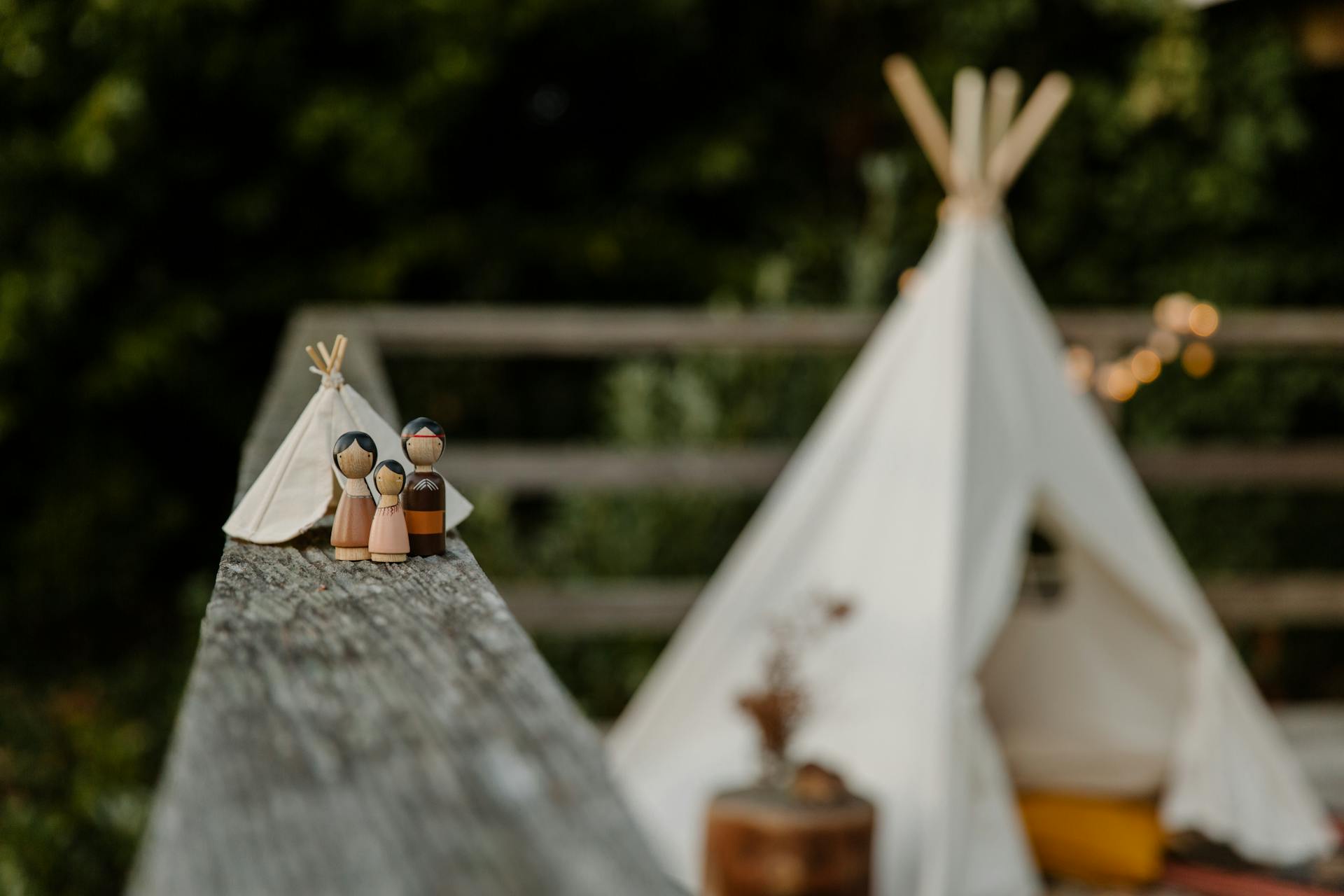 Handgjord miniatyr av äkta wigwam och form av familj i mjuk fokus placeras på trä räls av staket på terrassen mot suddig ursprungliga tält