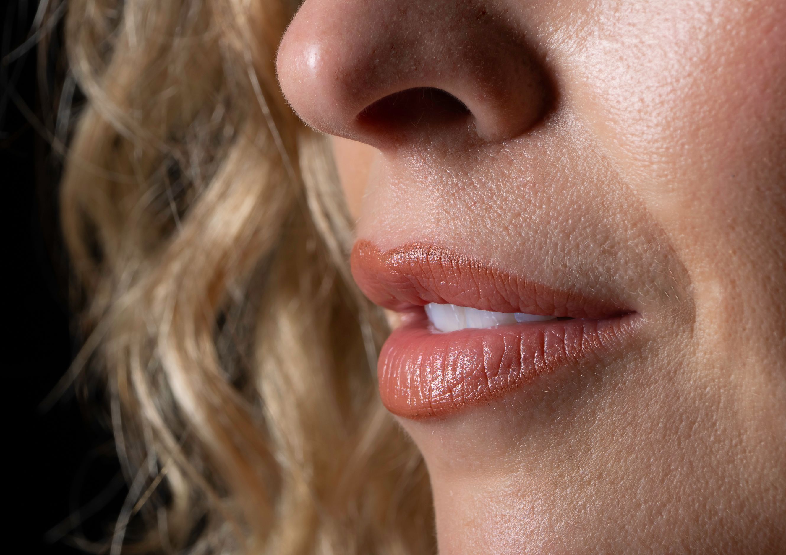 Detailed close-up of a woman's lips and nose with curly hair, emphasizing skin texture.