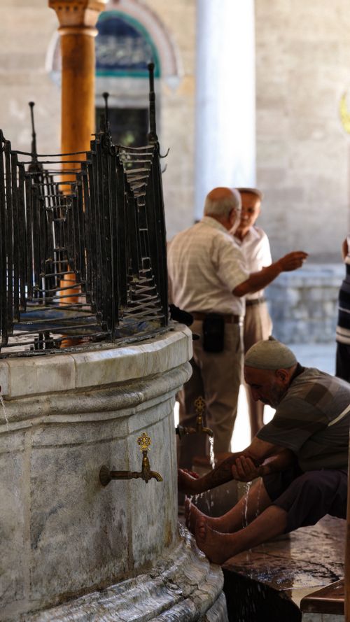 Free Men perform foot ablution at a historic fountain in a serene courtyard setting. Stock Photo