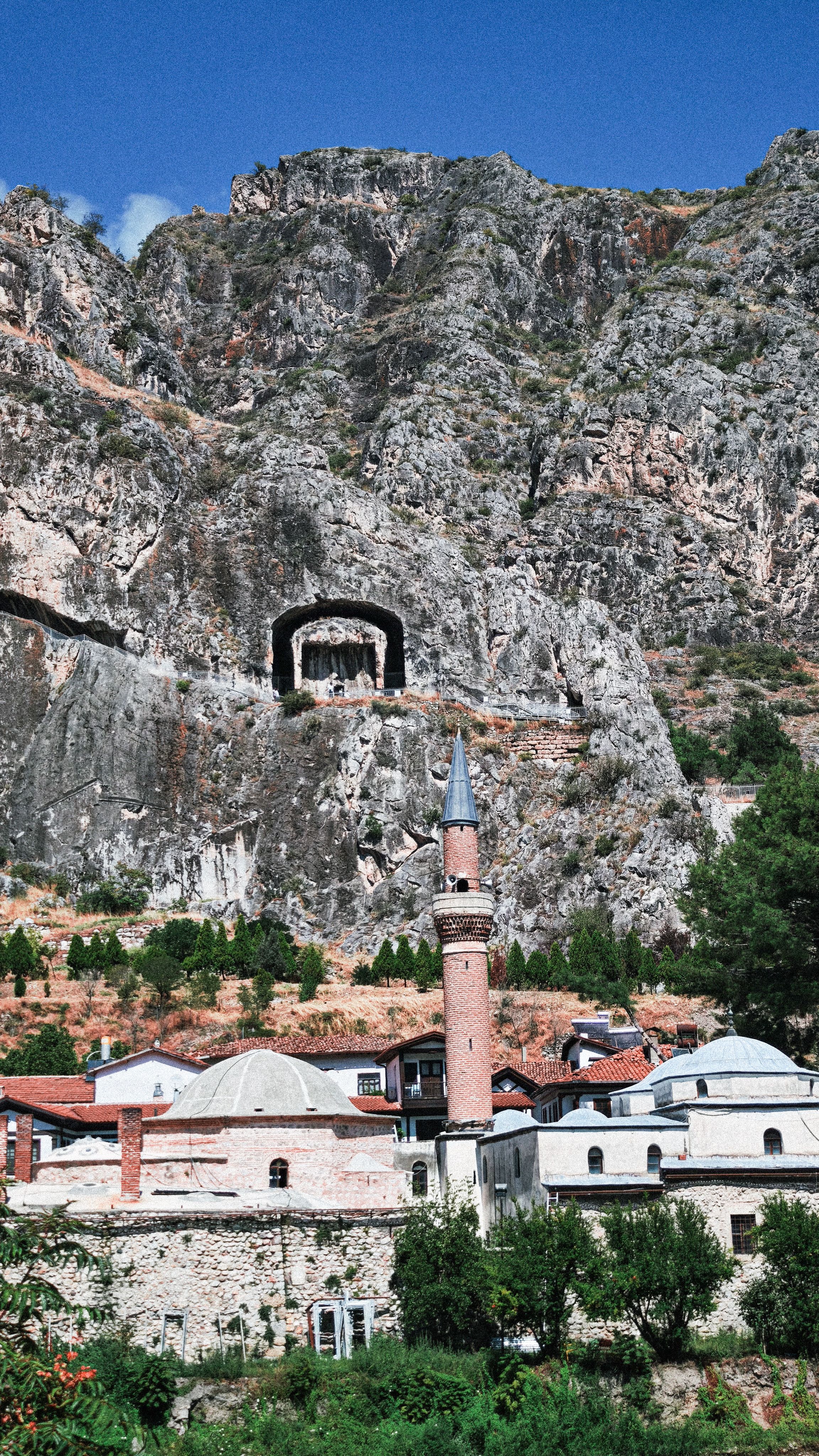 View of Amasya's ancient rock tombs and mosque against a mountainous backdrop.