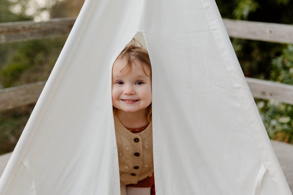 Free Happy little child smiling while peeking from tent Stock Photo