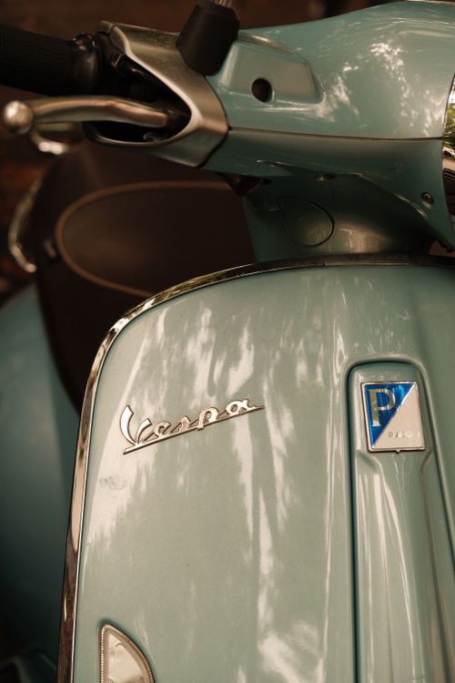 Free Detailed view of a vintage blue Vespa scooter outdoors, showcasing its iconic logo. Stock Photo