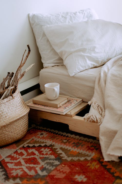 Free Comfortable cozy bedroom with bed wooden shelves with book and cup while wicker basket with sticks placed on ethnic styled rug Stock Photo