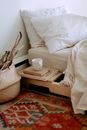 Comfortable cozy bedroom with bed wooden shelves with book and cup while wicker basket with sticks placed on ethnic styled rug