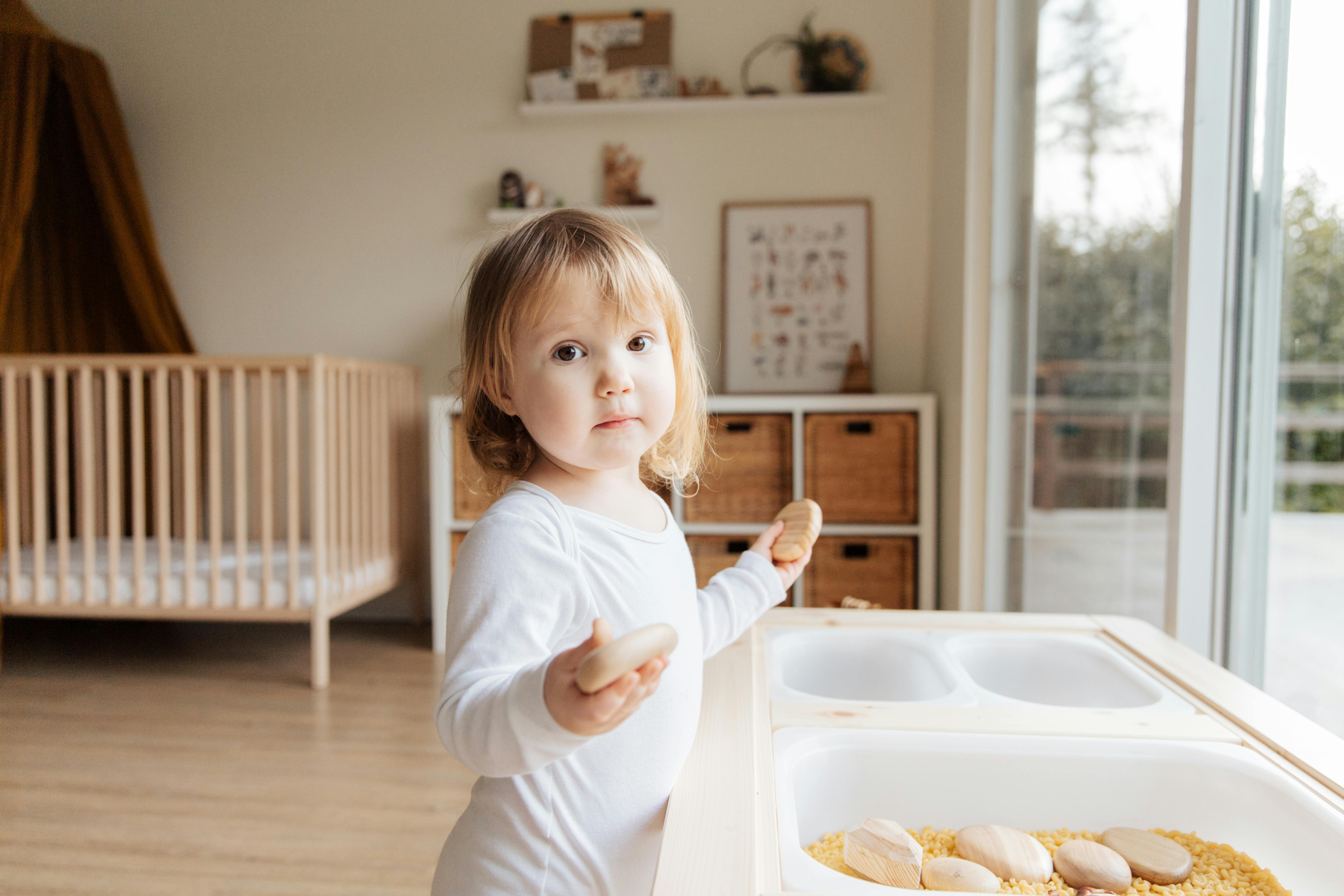 cute little girl playing with stones near plastic container at home