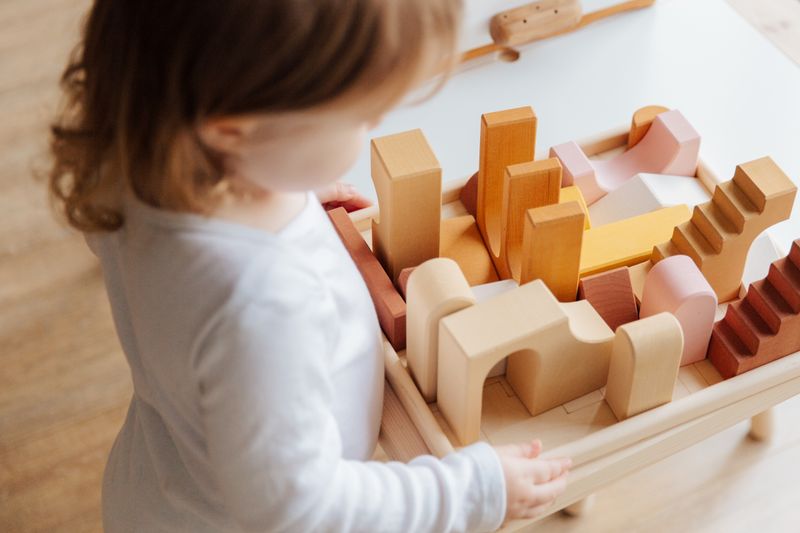 Toddler pushing a wooden walker cart across a bright playroom floor