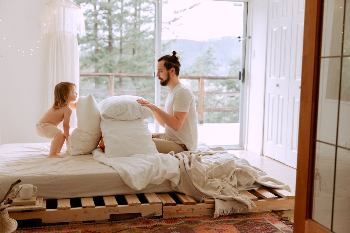 Father and kid playing with pillows in bed in light bedroom at home